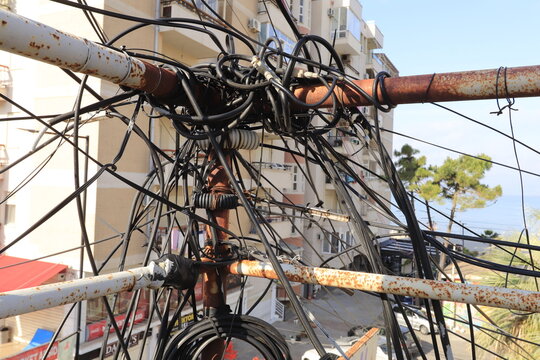 Urban infrastructure and power grid issues, tangled electrical wires and cables on a rusty pole in a city