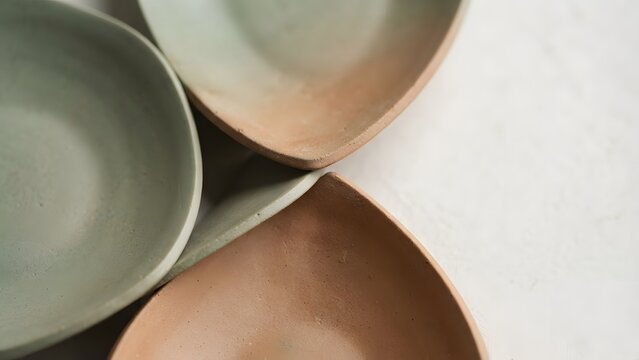 Close-up of three unique, organic-shaped ceramic dishes in pastel green and terra cotta colors, artfully arranged on a textured white surface.
