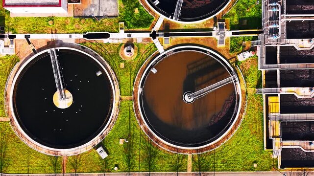 Top down view of circular sludge tank with bird. White bird float on dark water beside a second tank showing brown sediment and metal rake arm.