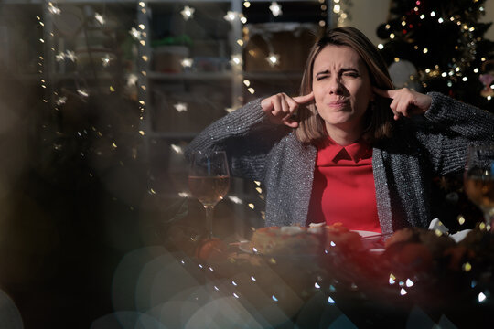   Irritated Woman Covering Her Ears Inside Loud Christmas Party Room. Annoyed lady blocks noisy festive music sitting at celebration festivity