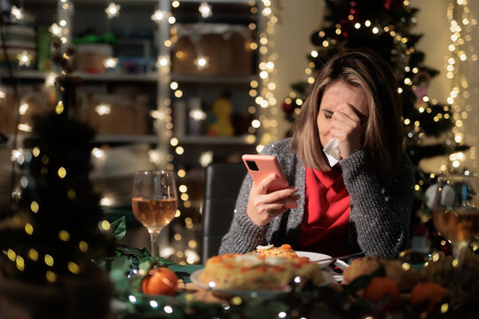 Sad Lonely Woman Crying Near Christmas Table Holding Her Smartphone. Upset lady weeps while reading bad text messages 