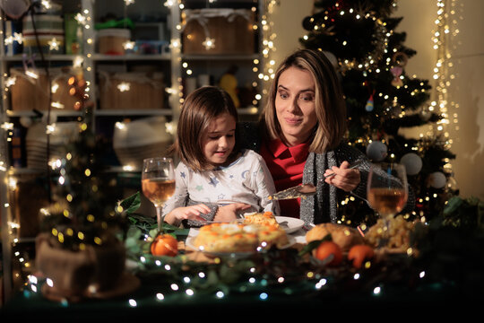 Happy Mother And Daughter Eating Traditional Boeuf Salad Near Christmas Tree. smiling family enjoys festive winter holiday dinner inside cozy decorated room background 