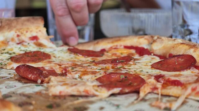 Close-up of hand picking slice from pepperoni pizza