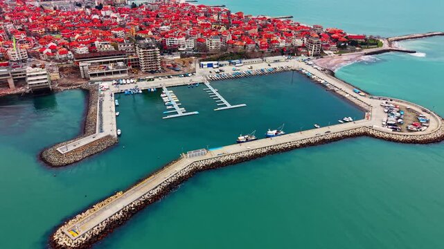 Aerial view of marina harbor and breakwater, Bulgaria. Floating dock hold small boat within a square shaped basin bordered by stone jetty and red roofed town.