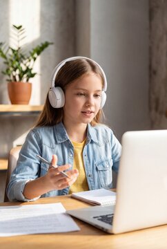Schoolgirl attending online class with headphones and laptop at home