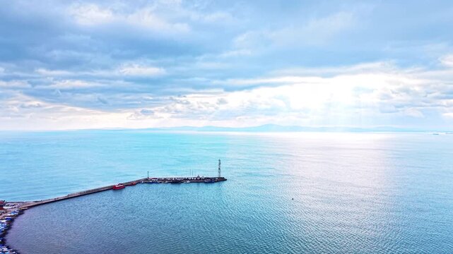 Panoramic view of a stone pier and lighthouse tower, Bulgaria. Aerial drone perspective of the Black Sea under a cloudy sky with distant mountains.
