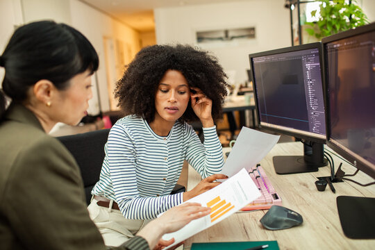 Two coworkers reviewing analytics at dual monitors in modern office