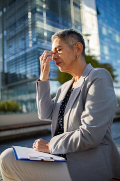 Senior businesswoman rubbing eyes outside office building