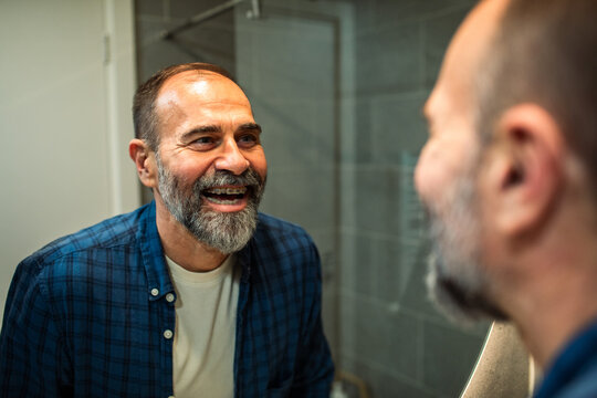Mature man with braces smiling at bathroom mirror