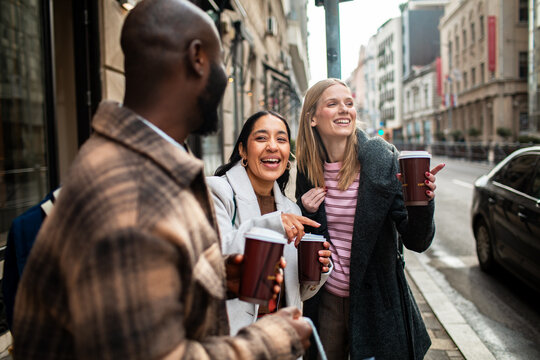 Friends laughing with takeaway coffee on city street