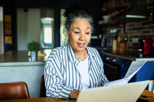 Senior woman reviewing bills on laptop in home kitchen