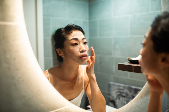 Woman applying facial mask in home bathroom mirror