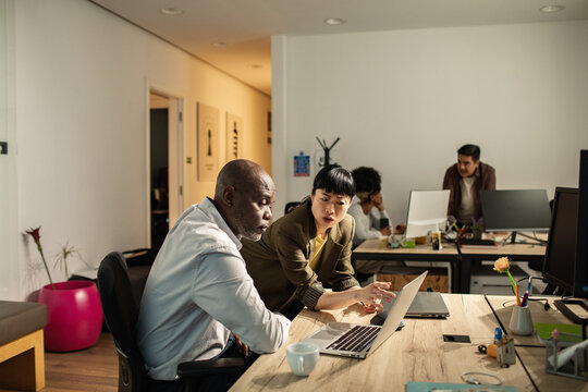 Coworkers collaborating on laptop in modern open office