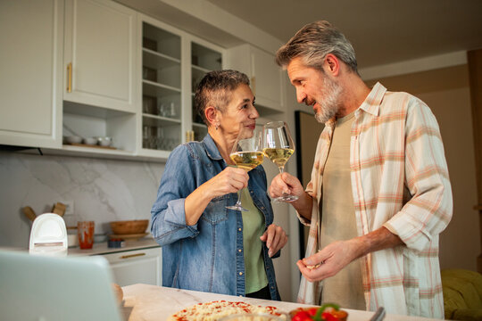 Happy senior couple toasting white wine in home kitchen