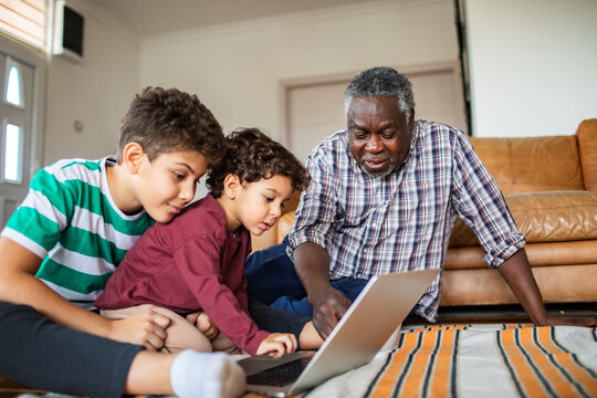 Grandfather teaching grandsons on laptop in living room