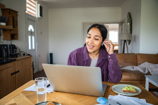 Young woman working remotely on laptop at a home kitchen table