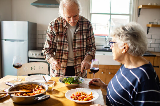 Senior couple enjoying pasta and wine in a home kitchen
