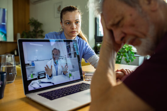 Caregiver supports senior man during telemedicine consultation at home