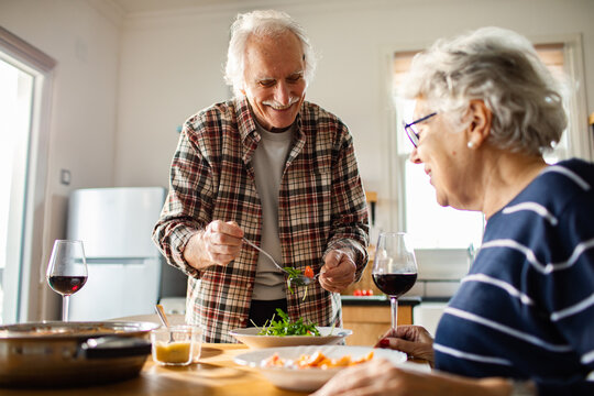 Smiling senior couple sharing salad in home kitchen