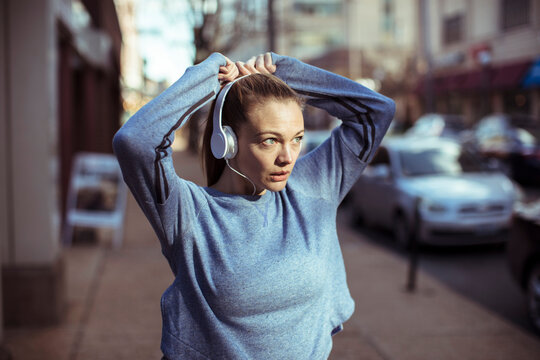Focused woman with headphones preparing to run on city street