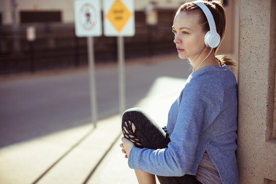 Young woman resting with headphones on city sidewalk