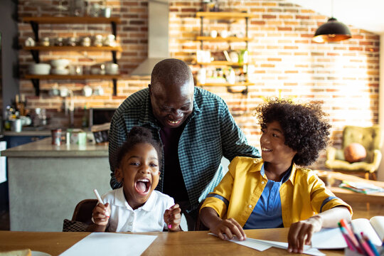 Father helping children with homework at home kitchen table