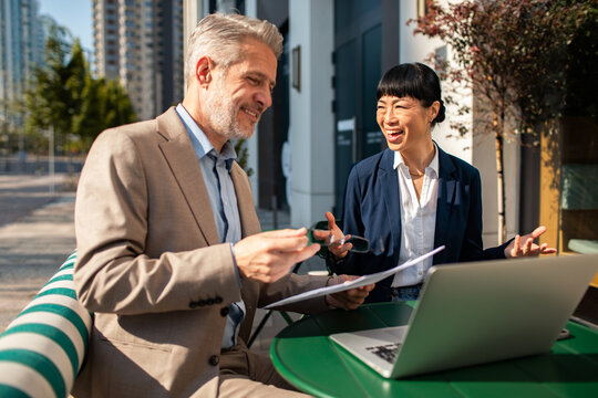 Two business colleagues reviewing documents with laptop at outdoor cafe