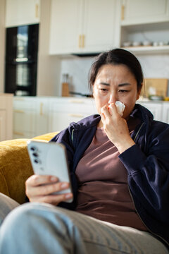 Concerned woman with tissue looking at smartphone at home