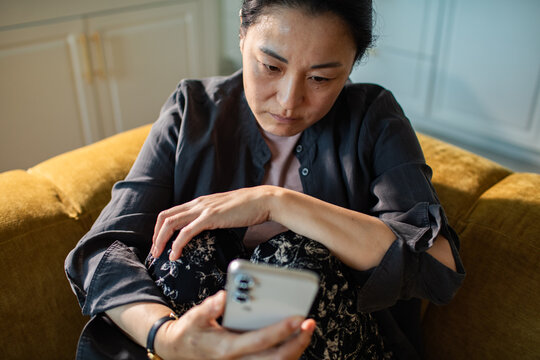 Concerned woman looking at smartphone at home