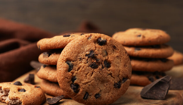 Stack of fresh homemade chocolate chip cookies with rustic dark wooden background in macro focus shot featuring appetizing crumbly texture and sweet snack concept for bakery advertising