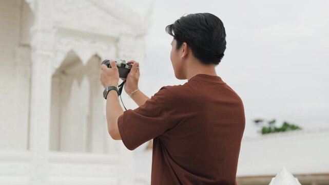 Attractive young Asian couple looking at digital camera pictures at beautiful white temple. Happy romantic tourist travelers enjoying historic sightseeing summer holiday vacation.