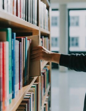 Discovering knowledge hand pulling a book from a library shelf symbolizing intellectual curiosity and the joy of reading in an educational environment