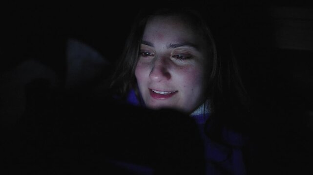 young Woman Playing Handheld Gaming Console While Relaxing on Bed at Home