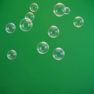 Translucent soap bubbles floating slowly upward against a solid green background.