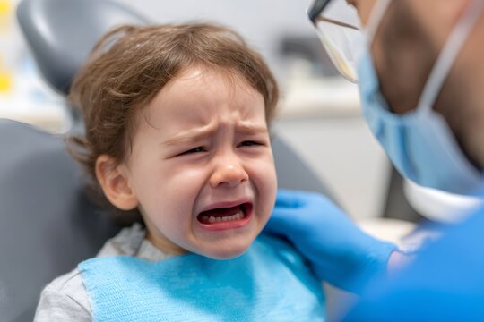 Crying child at the dentist office. Scared toddler boy in a dental chair during an examination with a doctor