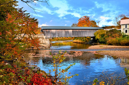 Rustic wooden covered bridge with beautiful autumn colors and river reflections at dusk, Vermont, USA