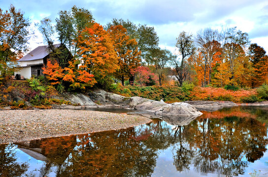 Beautiful river reflections in a calm river during autumn. Fall colors and old rustic house at dusk in Waitsfield, Vermont, USA