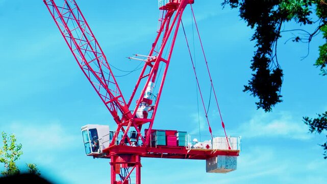 Close-up low-angle view of a bright red tower crane showing the operator cabin, machinery deck, and concrete counterweights