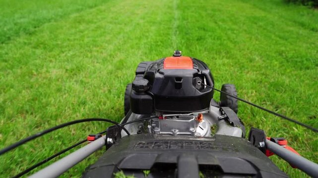 Lawn mower moves through vibrant green grass. Engine hums as blades cut fresh grass. Handlebars grip firmly as operator guides machine. Perfect for garden maintenance or outdoor activity projects