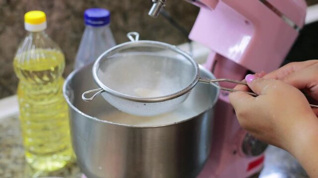 Sifting flour through a sieve into a mixer bowl while preparing homemade dough, an essential baking step in the kitchen alongside cooking oil