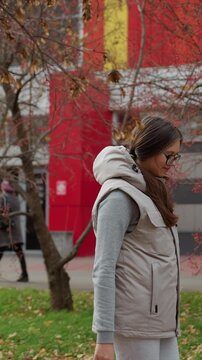 Subject is woman standing still at park area covered. Her head turns from one direction to another revealing. Environment features mix of natural elements like dry leaves