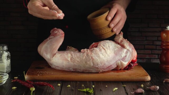 Chef in black apron seasons raw meat on wooden cutting board with spices from a clay bowl, showcasing a step-by-step process of preparing ingredients in a rustic kitchen setting