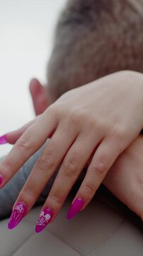 Nail art including ears rests gently upon man neck and leg. Nails show detailed white designs like bunny heads. Outdoor or indoor space with focused light emphasizes hand