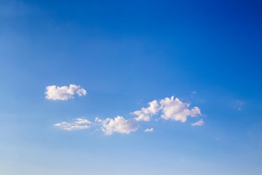 Rich blue sky with small white fluffy clouds on gradient background