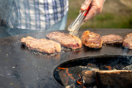 Hand flips sizzling steaks over glowing embers