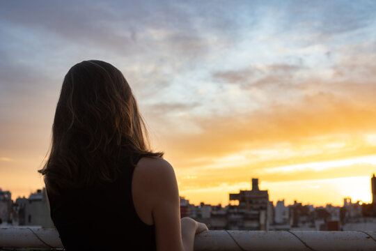 Thoughtful teenager observing sunset cityscape from urban rooftop