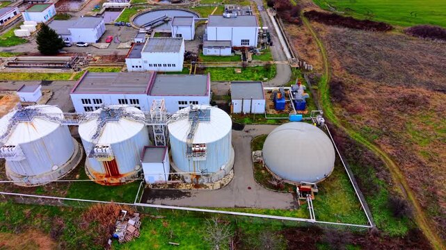 Elevated aerial view of wastewater treatment tanks, Bulgaria. Cylindrical digester towers, dome gasholder and white facility buildings with green surroundings.