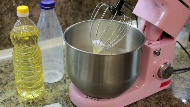 Pouring sunflower oil with a tablespoon into the mixer bowl, adding a key ingredient to the batter while preparing homemade dough for baking