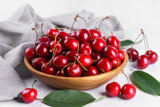 Fresh ripe red sweet cherries in wooden bowl with green leaves on light textured background. Healthy organic summer fruit, juicy red berries, natural freshness, healthy eating, seasonal food