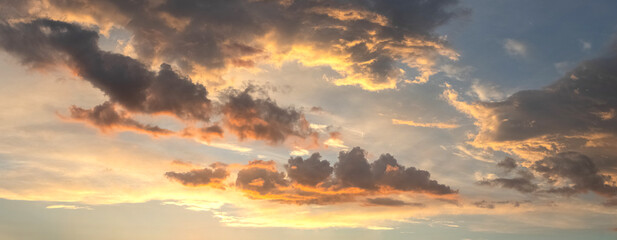 Obraz premium Dramatic sunset sky with scattered clouds illuminated by orange sunlight against blue background